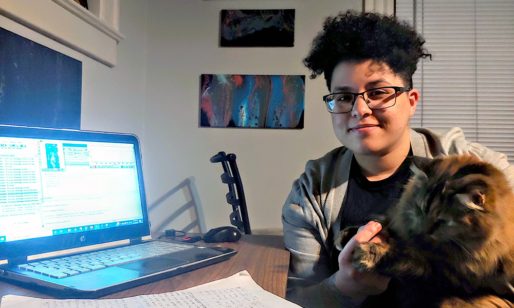 Tara Peña holds her cat while sitting next to her laptop.