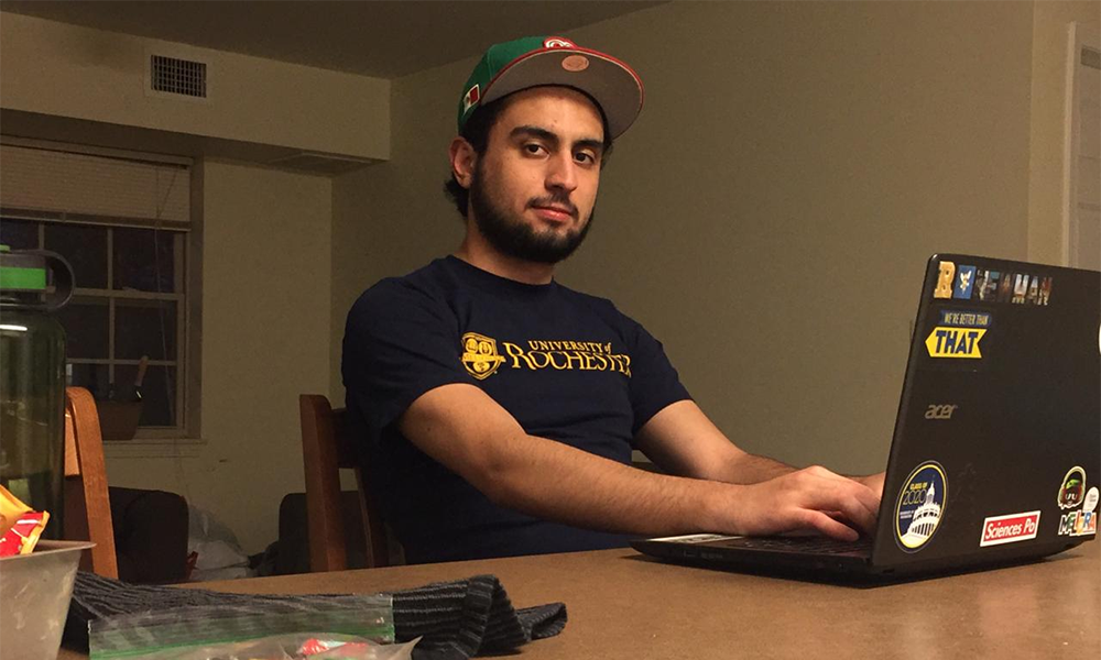Feature image Student at desk on laptop gazes at camera.