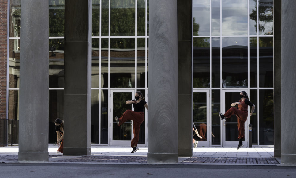 Dancers clad in red pants and black tops perform amid pillars.
