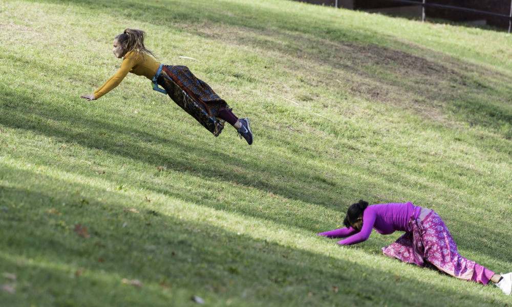 A dancer mid-air and another on the ground as they ascend a hill.