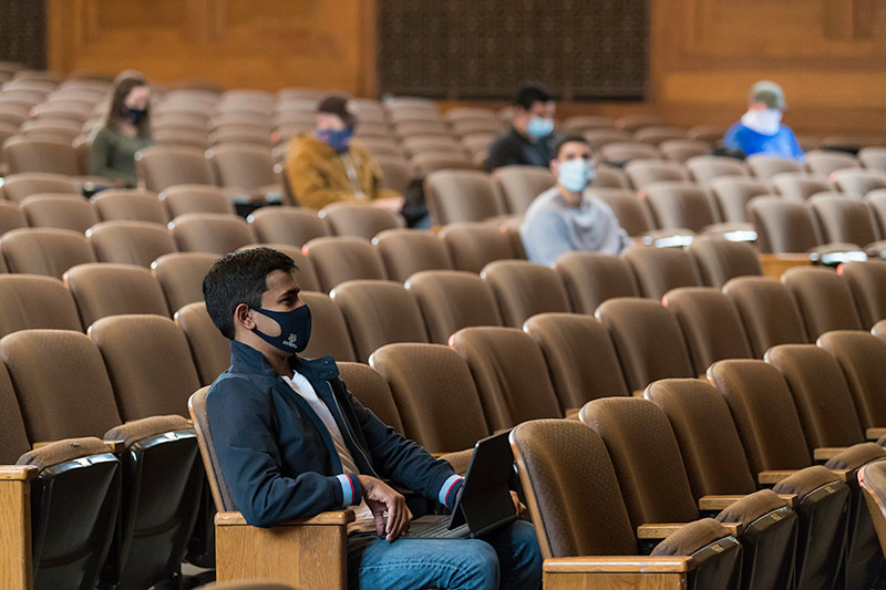 students sitting in large theater, socially distanced, wearing masks.