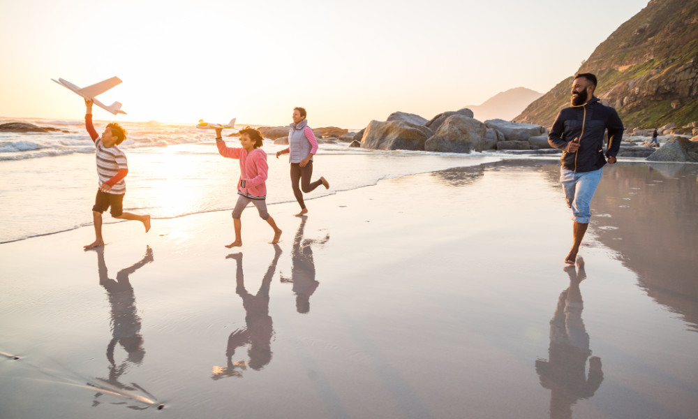 Happy family runs along the beach with toy planes to illustrate psychological flexibility.