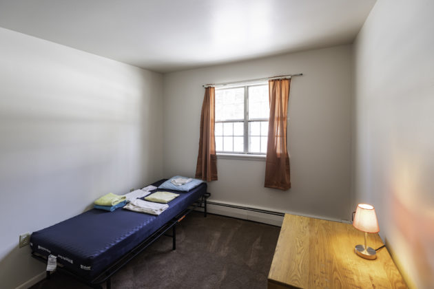 Single bed, desk, and lamp in room with window.