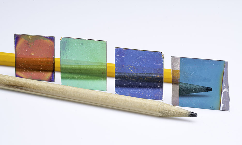 A pencil sits in front of four colored glass plates.
