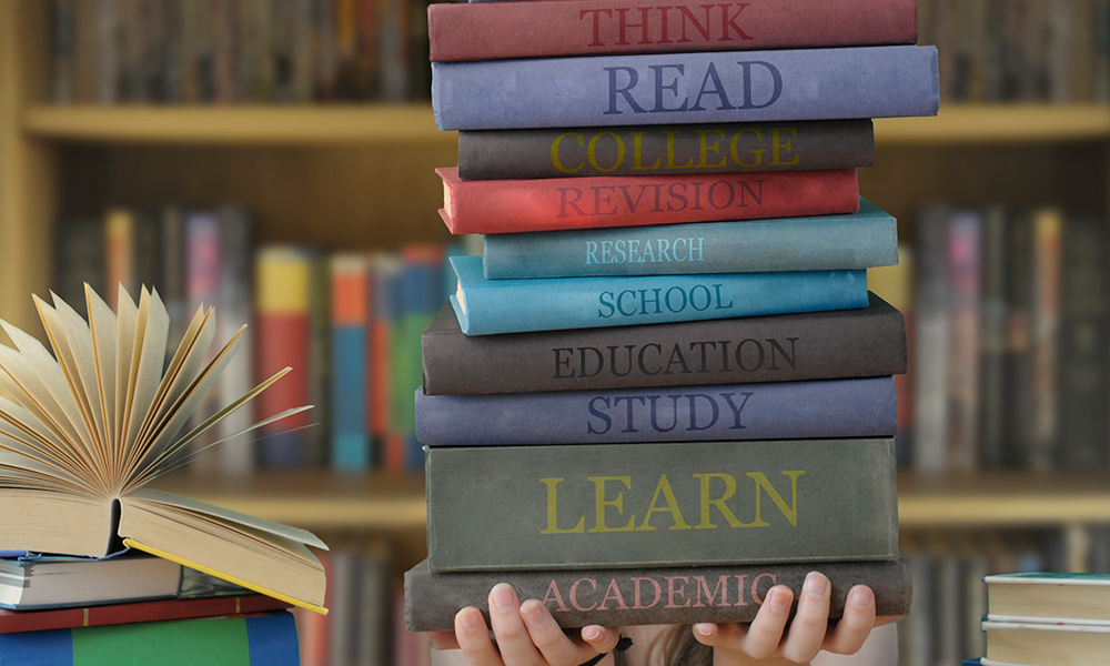 Young person's hands holding stack of books.