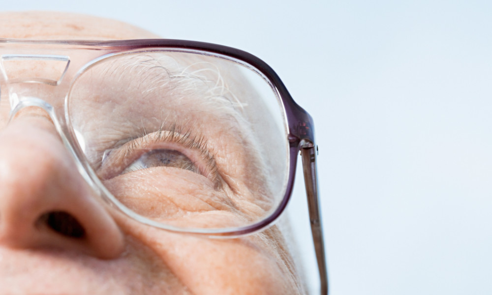 Senior man, half out of the frame, wears glasses and looks up with a light blue sky in background.