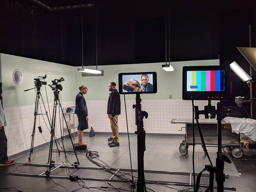 two actors on a set, surrounded by cameras and screens.