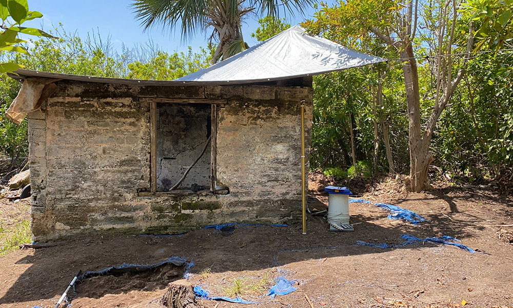 Feature image an archaeological digging site on Smith Island, with an old stone building in the forground and palm trees and ocean in the background.