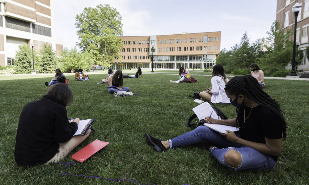 Feature image Ten masked and distanced students sit outside on the Hajim Quad lawn surrounded by red brick buildings and blue skies.