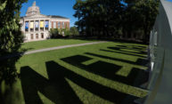 The Meliora letters cast a shadow on the Eastman Quadrangle lawn with Rush Rhees Library in the background.
