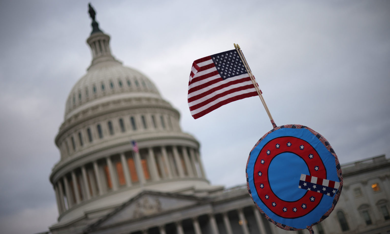 Circle sign with a Q and American flag on top with the US Capitol dome in the background.