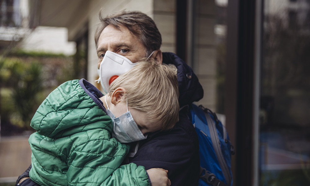 a man wearing a Covid mask holding a toddler wearing a surgical mask.