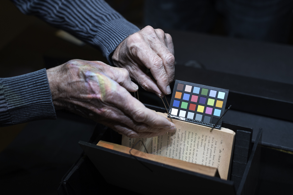 hands open a book halfway with a card filled with colorful squares next to it
