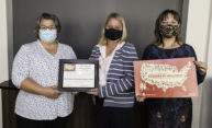 three women, wearing face coverings, stand together holding signs