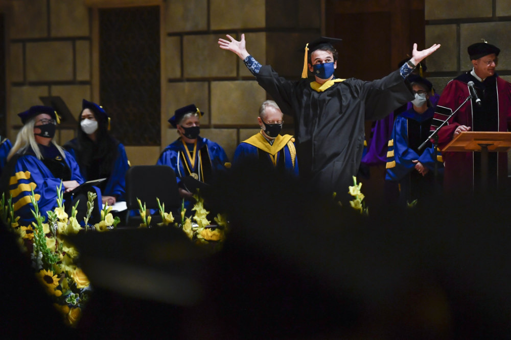 Class of 2020 graduate walks across the stage with arms raised as part of commencement.