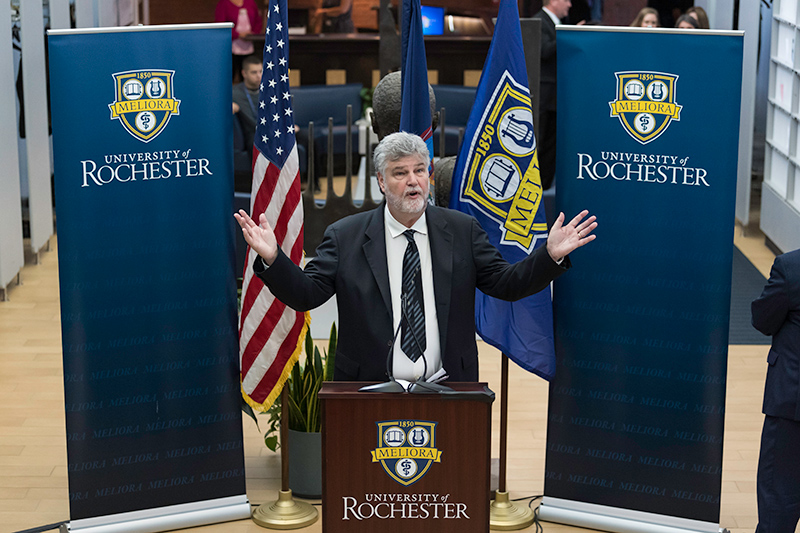 Michael Campbell speaking at a press conference behind a podium with a University of Rochester logo.