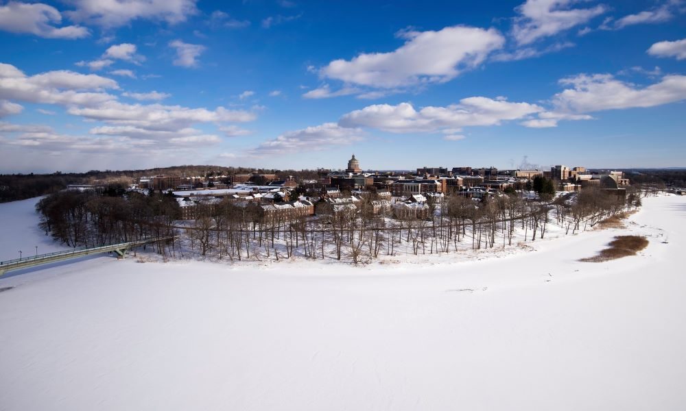 Snow-covered River Campus and Genesee River with blue skies and white clouds overhead.