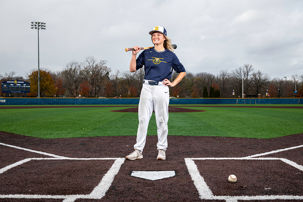 Beth Greenwood stands at home plate and smiles, a bat over her shoulder.