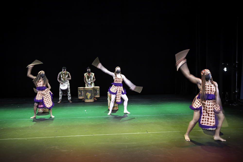 three students dance in the foreground while two people play drums in the background
