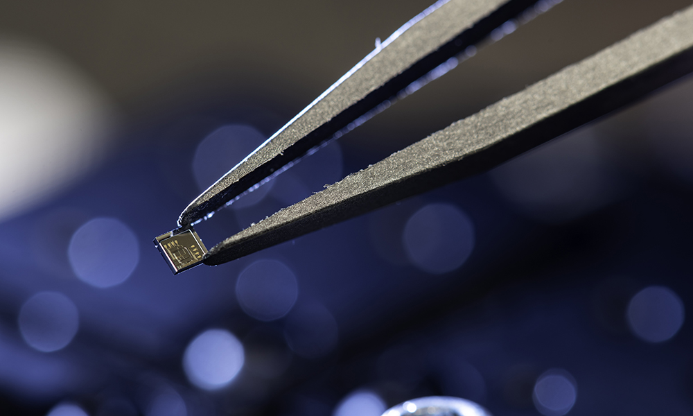 Closeup of tweezers grasping tiny chip.
