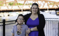 A mother and her son, who has FASD, pose for a photo near the Erie Canal with a bridge in the background.