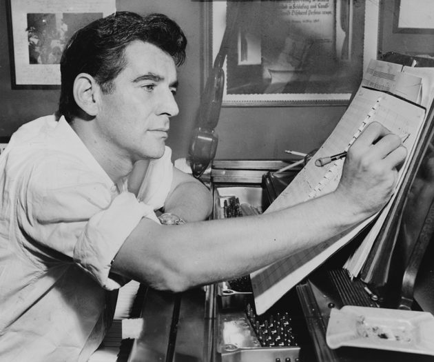 leonard bernstein sits at the piano and makes a notation on sheet music