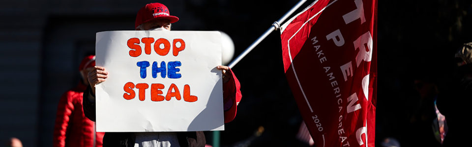 protester carrying a sign that says STOP THE STEAL and a Trump-Pence flag.