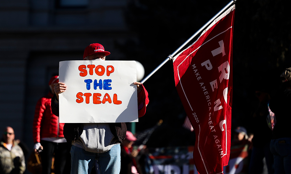 protester carrying a sign that says STOP THE STEAL and a Trump-Pence flag.