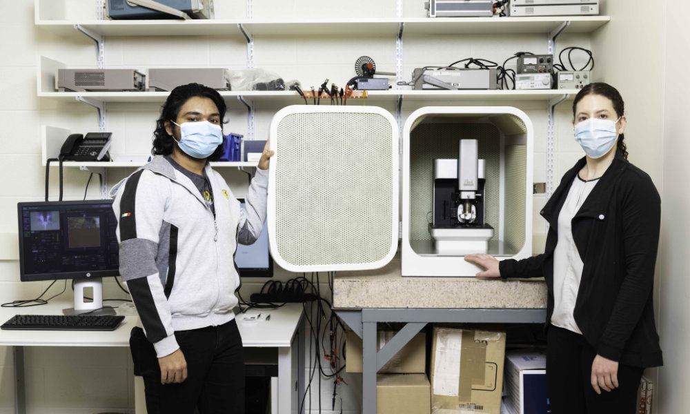 Two masked researchers stand next to an atomic force microscope.