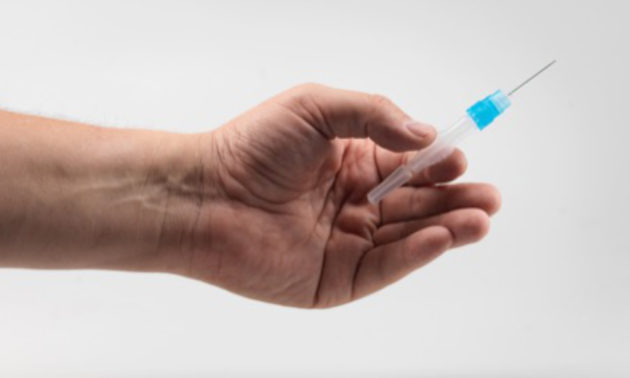 close-up of hand holding a small syringe.