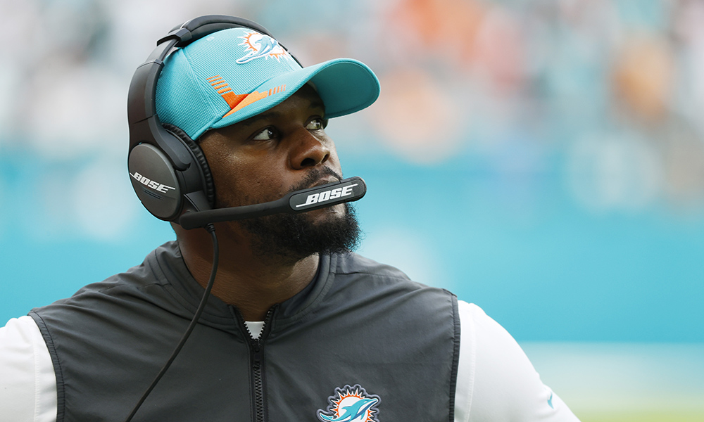 Feature image coach Brian Flores wearing a baseball cap and headset looks off into the distance.