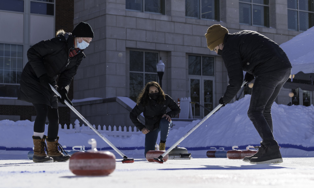 Three students curling on campus during the winter.