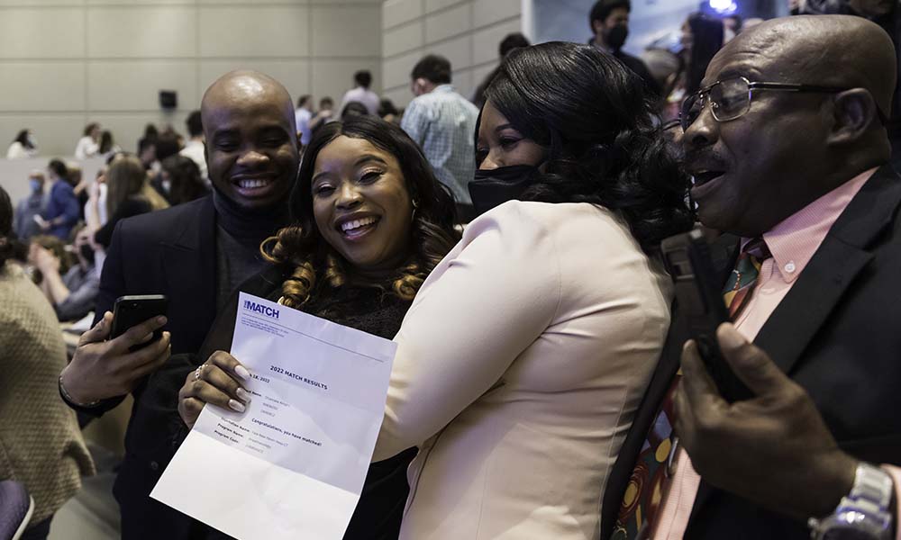 Feature image Medical student, standing next to boyfriend and parents, smiles and shows letter.