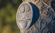 Closeup of Meliora medallion carving at the base of a campus flagpole.
