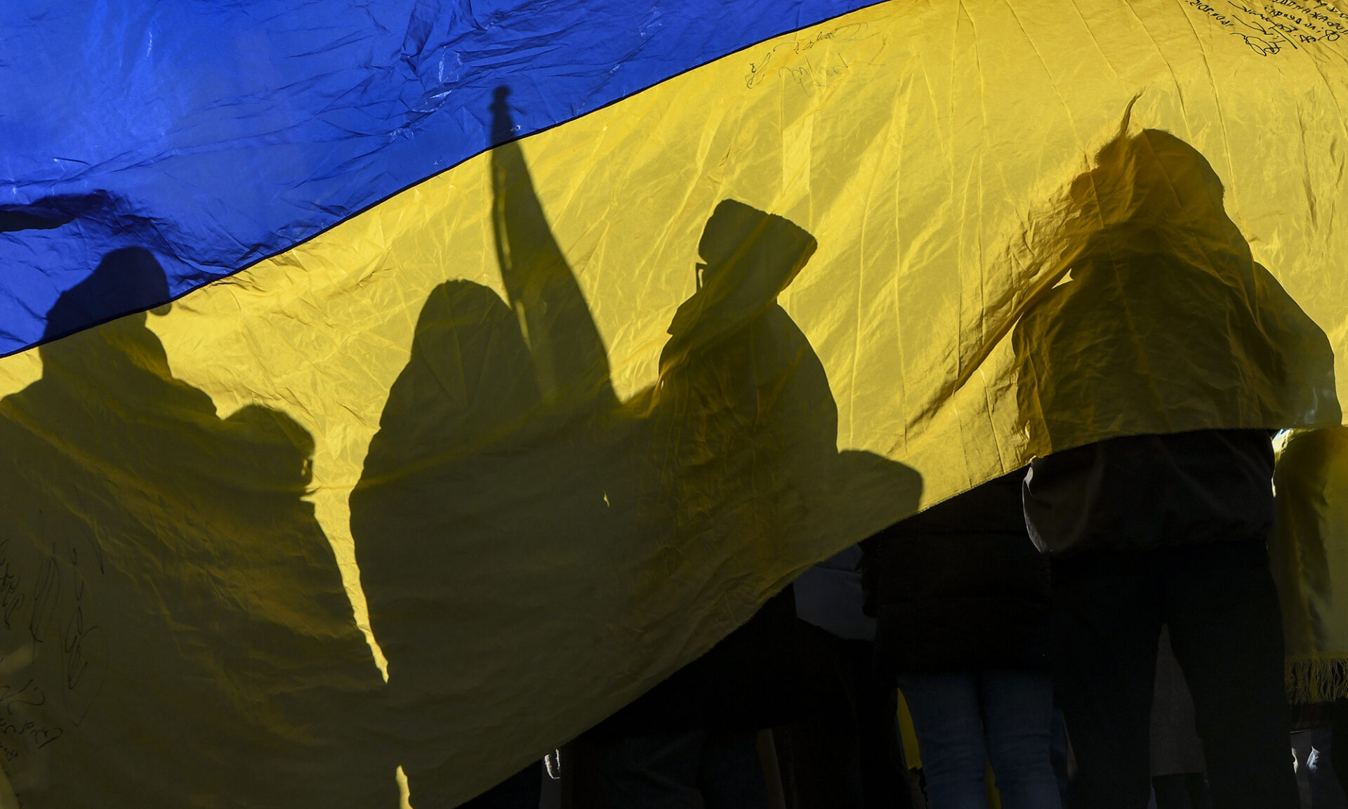 protesters holding signs, viewed through a Ukrainian flag.