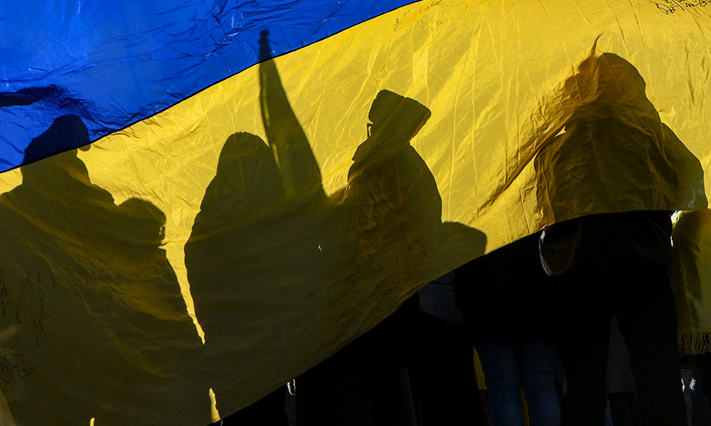protesters holding signs, viewed through a Ukrainian flag.