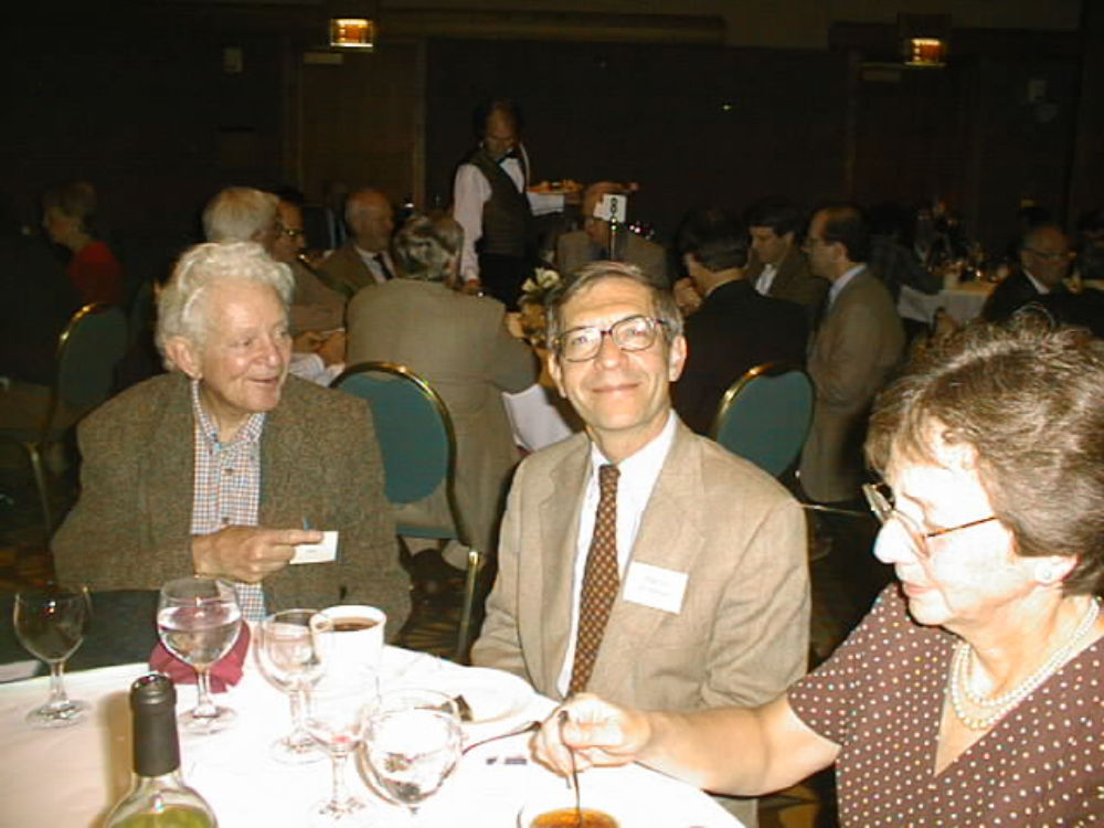 Leon Lederman, Tom Ferbel, and Tom's wife Barbara seated at a table.