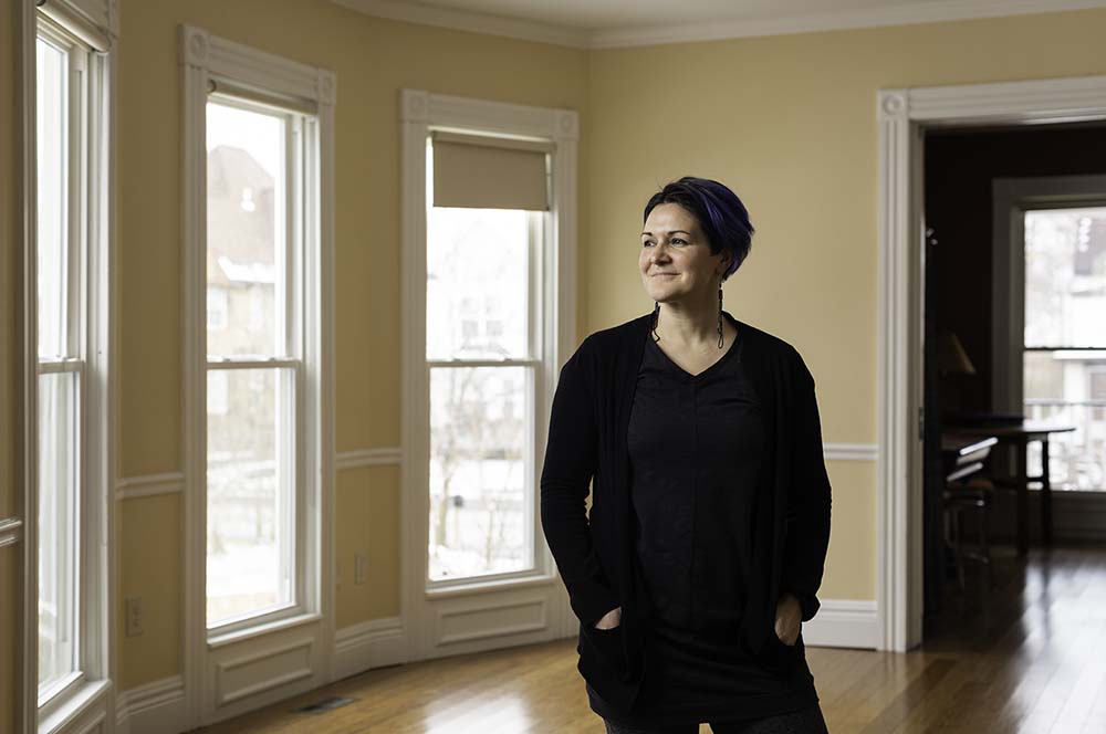 Gwen Olton standing in sunlit room, smiling and gazing to her right.