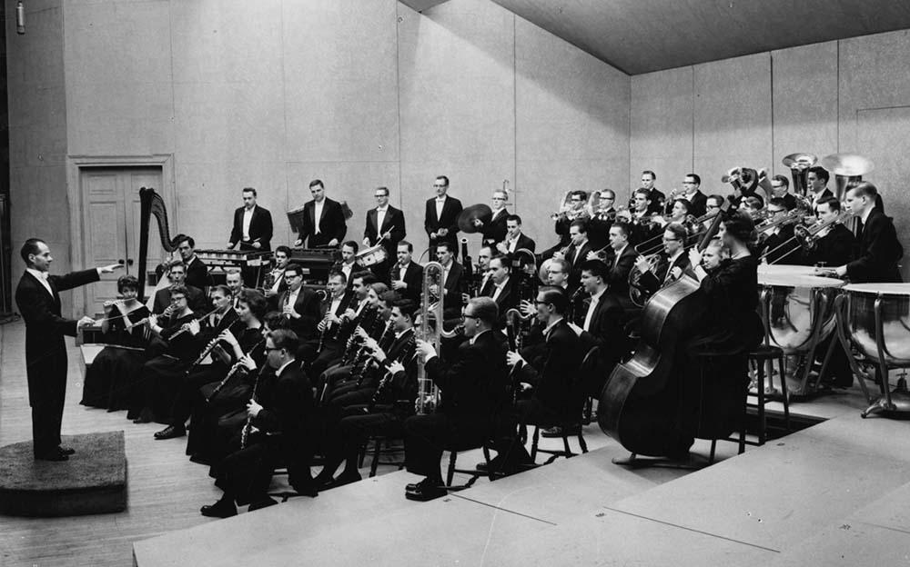Black and white archival photo of conductor leading wind ensemble in dress rehearsal.