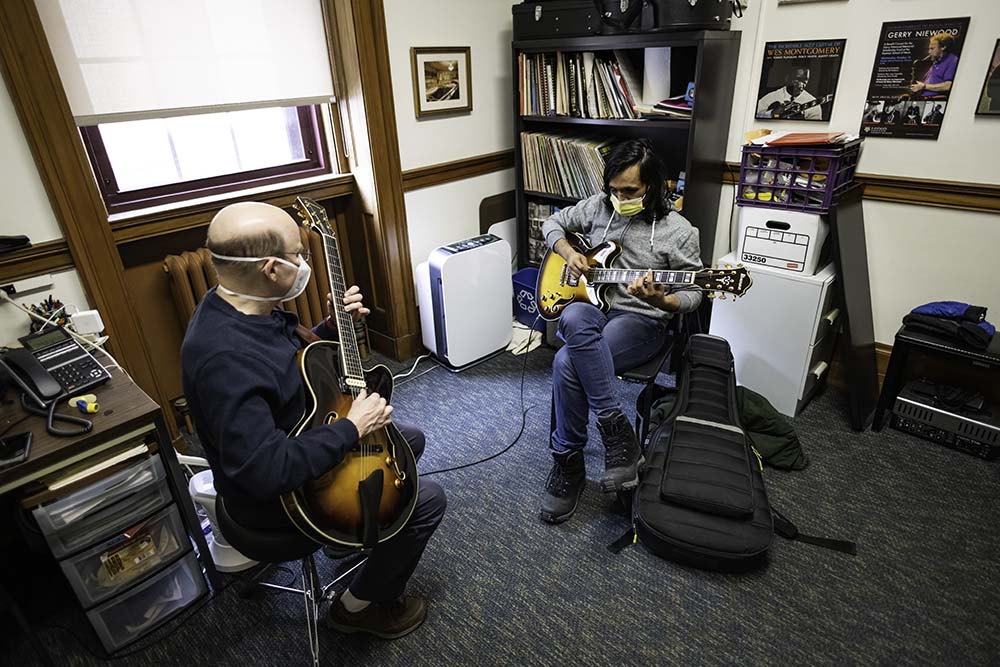 Eshaan Sood and instructor Bob Sneider seated across from one another, strumming guitars in office.