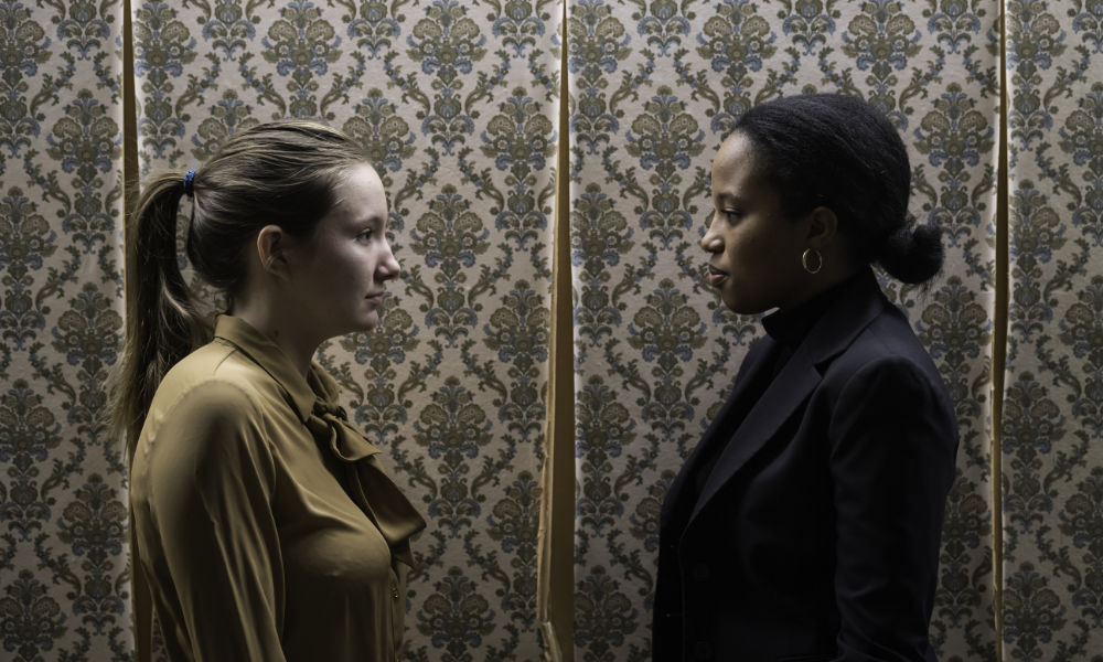 Feature image Two actors in a production of Marisol face each other in profile against a wallpapered background.