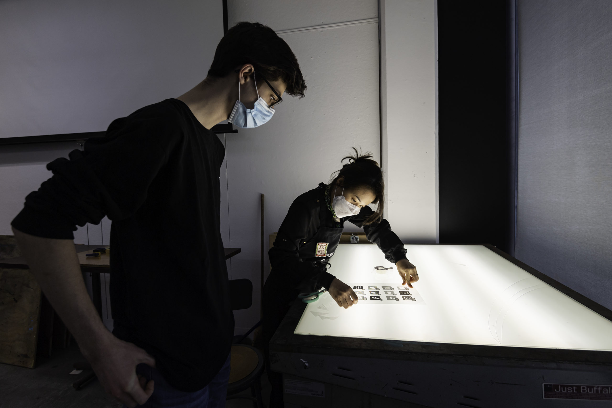 professor and student wearing covid masks lean over a light table