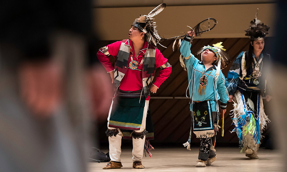 Feature image Two dancers, one an adult and one a child, dressed in traditional Native American dress perform in Wilson Commons.