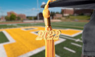 Class of 2022 graduation cap and tassel closeup with Fauver Stadium's "Spirit R" in the background.