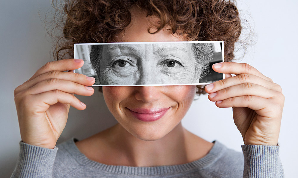 a young woman holds a photo of an older woman's eyes in front of her face.