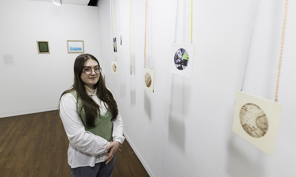 student stands beside small circular art prints hanging from strings.