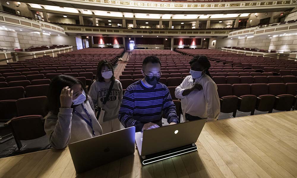 Two people work on laptops on stage while two others watch.