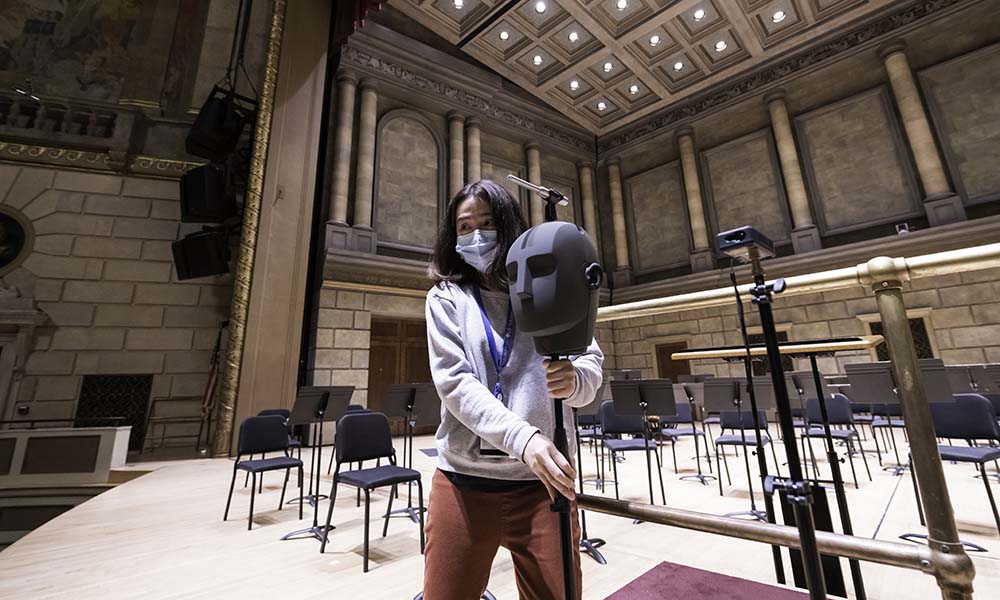 Woman adjusts position of a synthetic human head affixed to a stand and placed on stage.