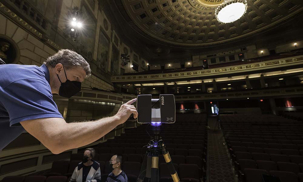 Man leans toward laser scanner affixed to tripod.