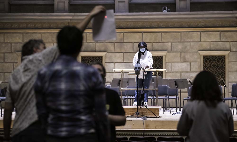Woman on stage points laser, shown as a red dot, toward a piece of paper.